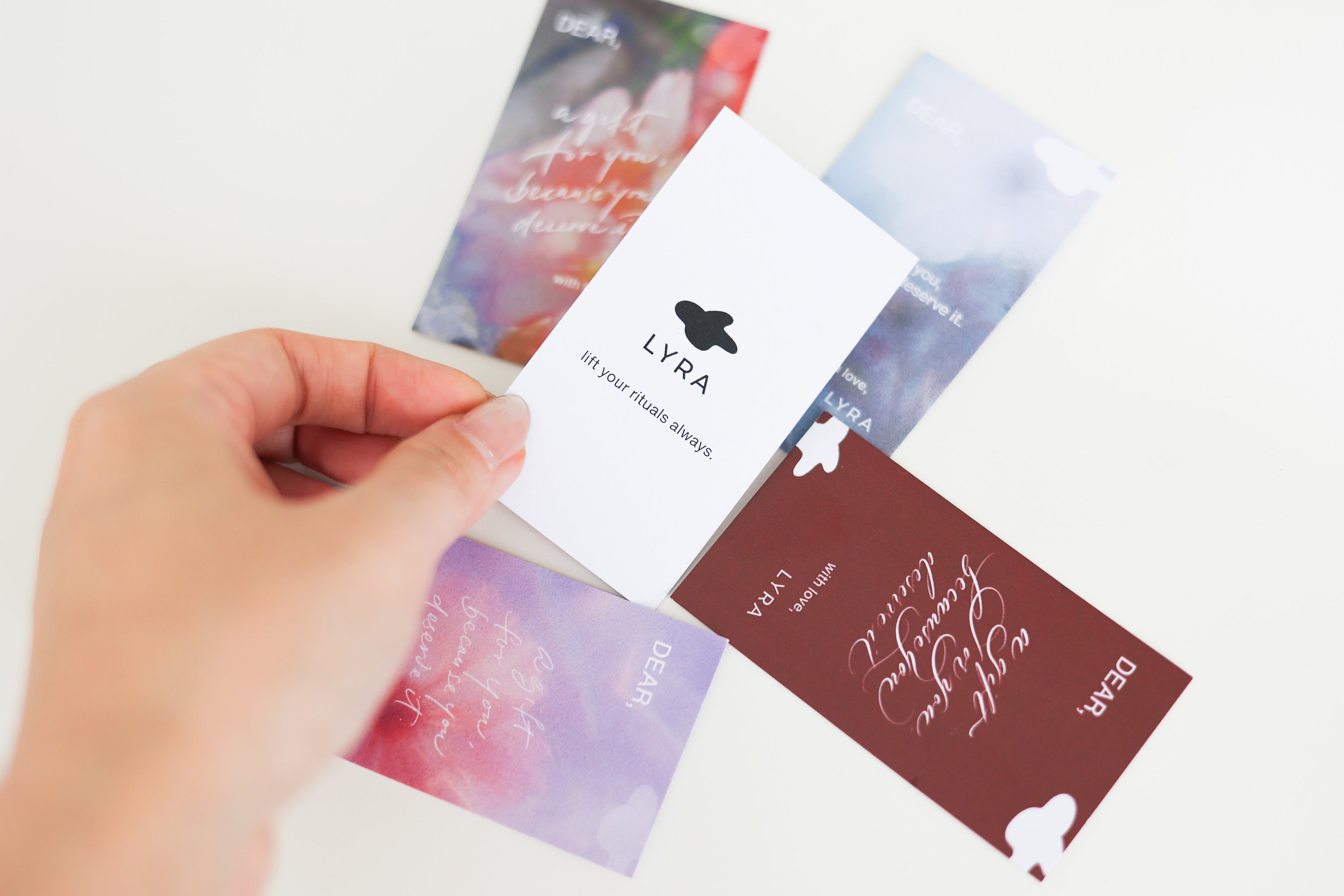 Hand holding a card with 'LYRA' branding over other branded cards on a light background